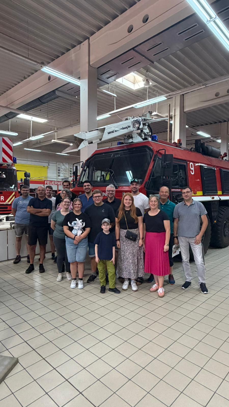 Gruppenbild vor einem Feuerwehrfahrzeug mit Drehleiter in der Fahrzeughalle des Museums