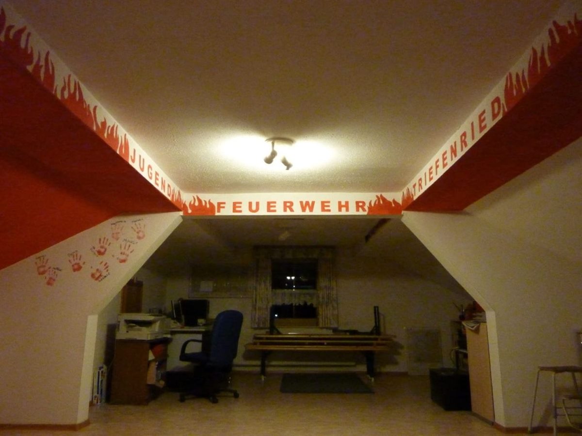 Blick in das Jugendzimmer mit Schreibtisch, Sitzbänken und den Handabdrücken der Jugendgruppe an der Wand